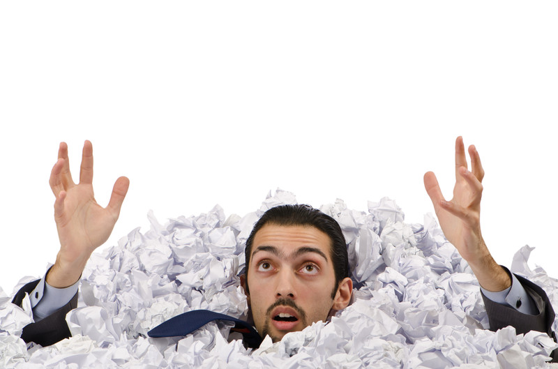 man being buried under mounds of crumpled paper
