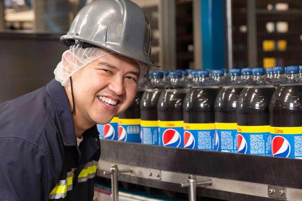 factory worker smiling next to bottled products on the assembly line